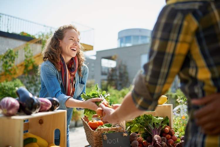 a woman smiles and buys vegetables from a farmer's market