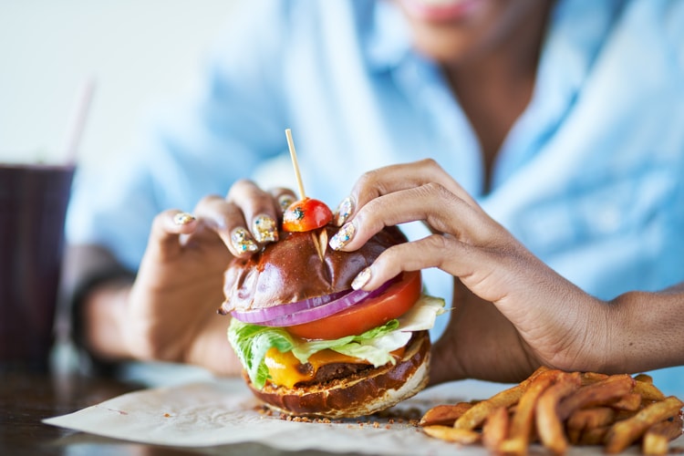 a restaurant patron picks up a burger and prepares to take a bite