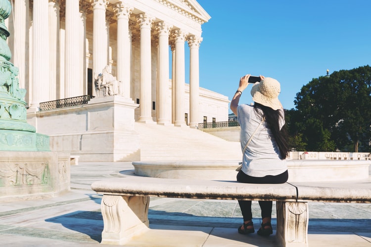 a woman points her phone towards the supreme court building to take a picture