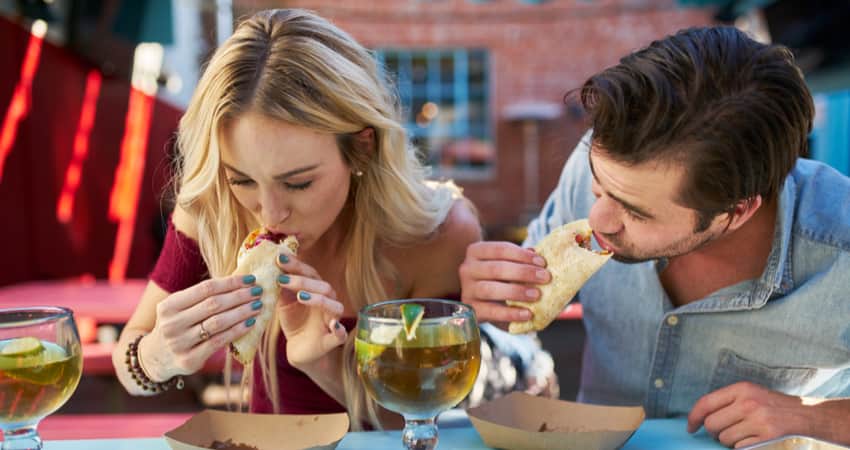 Two people eating tacos with cocktails 
