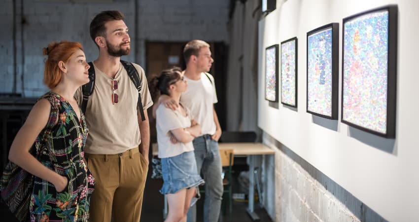 A group of museum goers consider paintings in a gallery