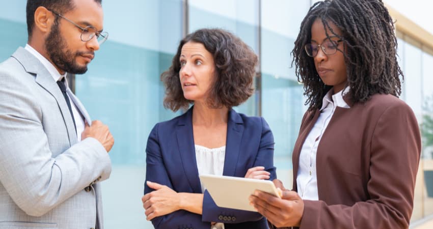 Three people discussing business over a tablet