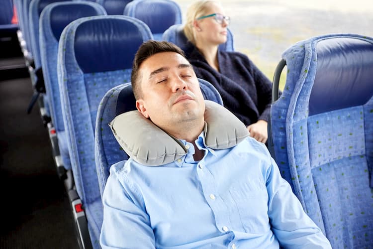 Employee resting on shuttle bus with neck pillow during evening rush hour commute.