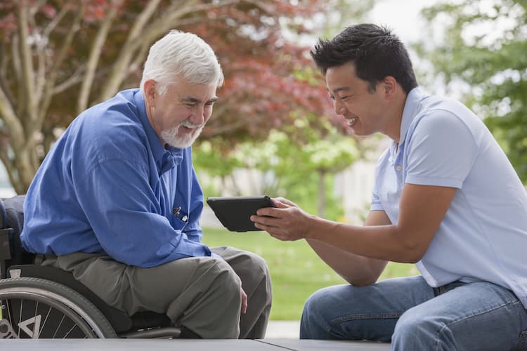 Older man in wheelchair talking to younger man with tablet