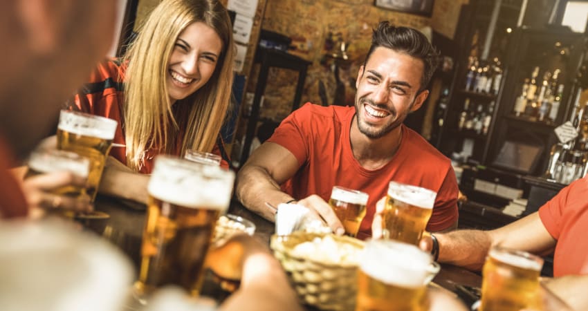 A large group sits at a table in a brewpub with glasses of beer set on the table