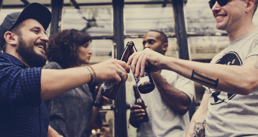 Four friends toast with bottles of beer in an industrial warehouse