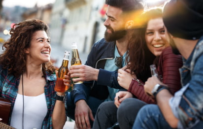 Four friends sit in an outdoor dining space and smile over bottles of beer