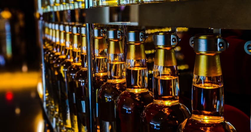 A row of bottles filled with amber-colored drinks in a dark metal mechanism