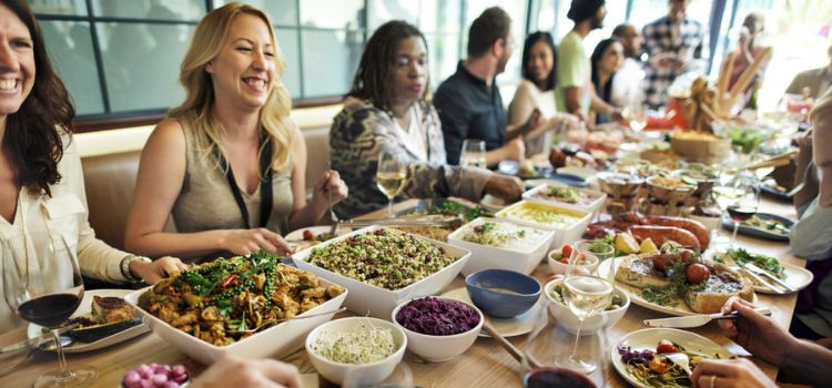 a diverse group of fifteen or more people enjoying a family style meal at a long table