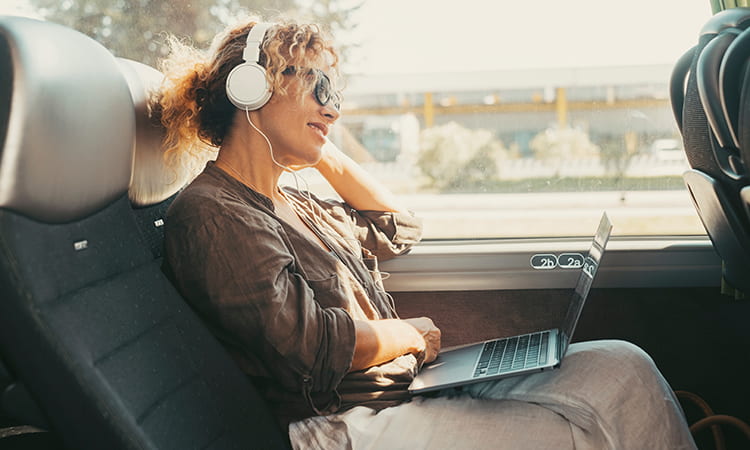 A woman with headphones types on a laptop aboard a charter bus