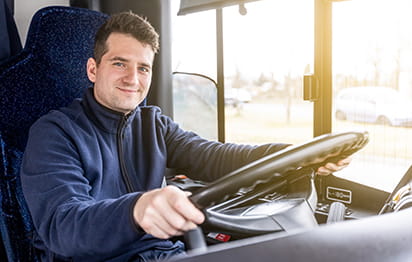 A male bus driver smiles while holding the wheel of a motorcoach