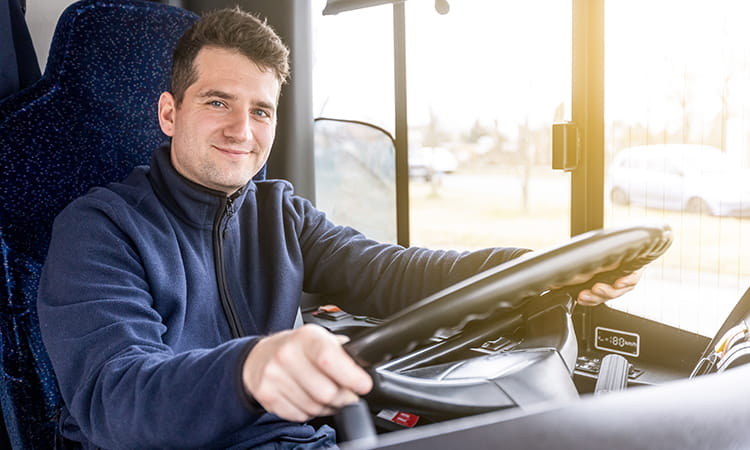 A male bus driver smiles while holding the wheel of a motorcoach