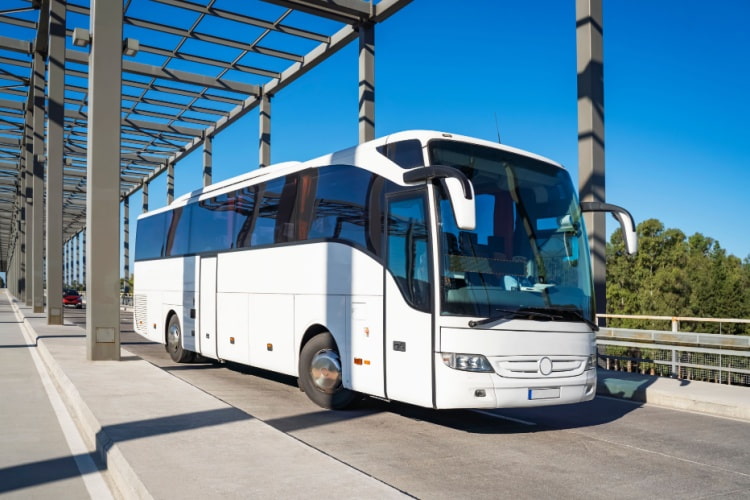 a plain white charter bus drives across a large bridge