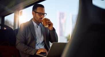 A man works on his laptop while riding on a charter bus to work